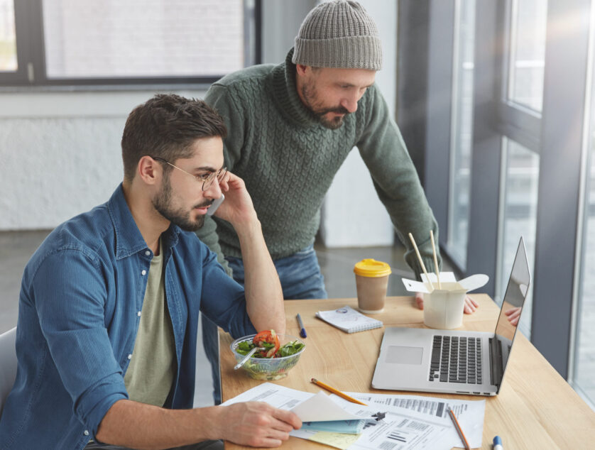 Experienced bearded male and his trainee develop new strategy together, work on improvement business affairs, study information from laptop, ask consultation in colleagues have dinner at office Experienced bearded male and his trainee develop new strategy together, work on improvement business affairs, study information from laptop, ask consultation in colleagues have dinner at office