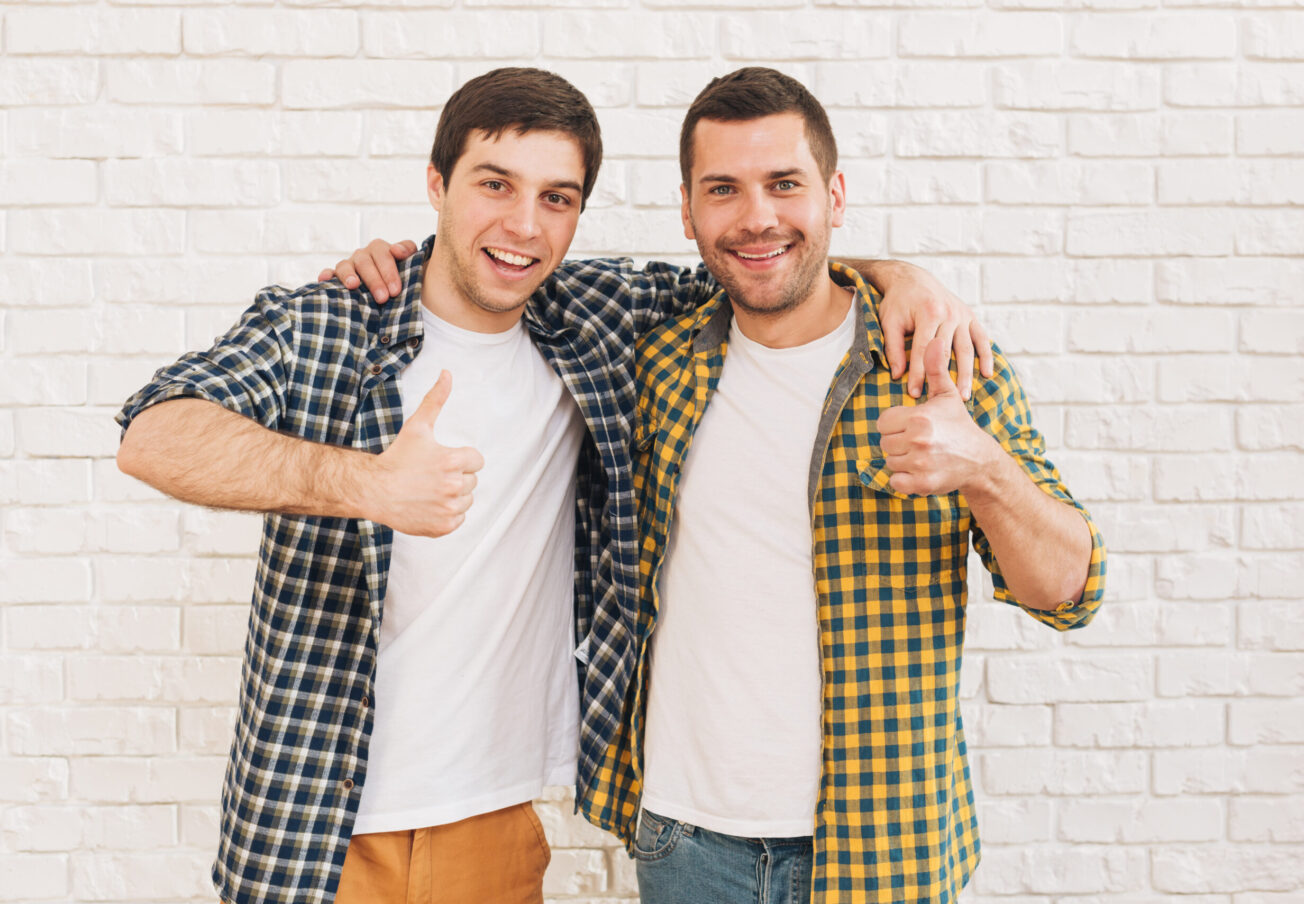 smiling-young-men-with-their-arms-around-their-shoulder-showing-thumb-up-sign