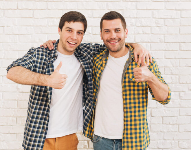 smiling-young-men-with-their-arms-around-their-shoulder-showing-thumb-up-sign